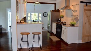 A kitchen with a central island, bar stools, a refrigerator, a stove, and hanging utensils.