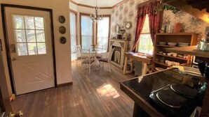 A cozy kitchen with a wooden floor, a dining area with chairs, a fireplace, and a kitchen counter with appliances. - The Victorian Cottage at Hamilton Creek (Burnet County)