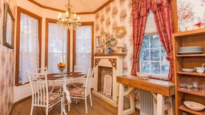 A dining area with a wooden table, white chairs, a chandelier, and a fireplace. - The Victorian Cottage at Hamilton Creek (Burnet County)