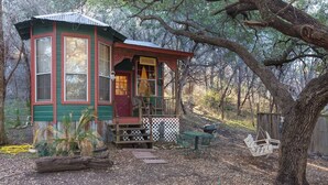 A rustic cabin with a porch, surrounded by trees. - The Victorian Cottage at Hamilton Creek (Burnet County)