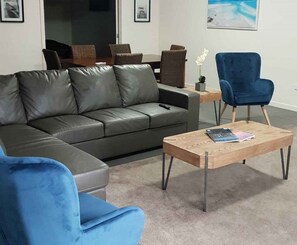 A modern living room with a grey leather sofa, a blue armchair, and a wooden coffee table. - Unit 2-83 Thompson Avenue, Cowes, Spacious 2 bedroom Unit, includes linen. (Cowes)