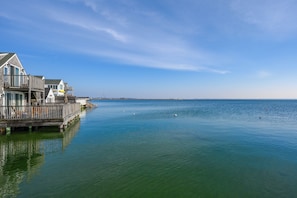 Une propriété située au bord de l’eau, avec une jetée en bois s’étendant sur une étendue d’eau calme, un ciel dégagé et une côte lointaine.