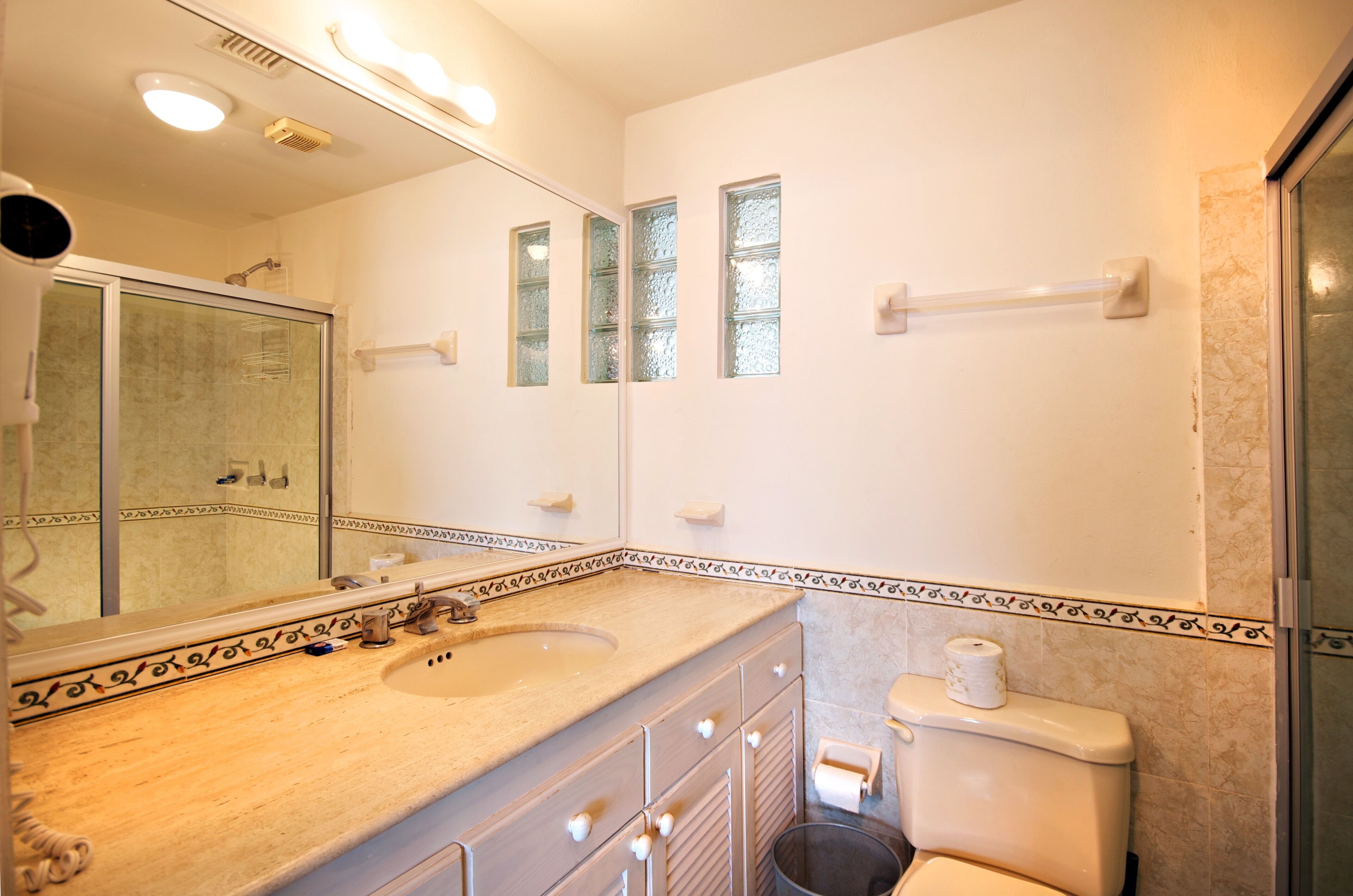 Un baño con un espejo grande, lavamanos, inodoro y zona de ducha.
