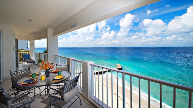 Een balkon met een eettafel, met uitzicht op een strand en helder turquoise water, en een vergezicht op de oceaan.