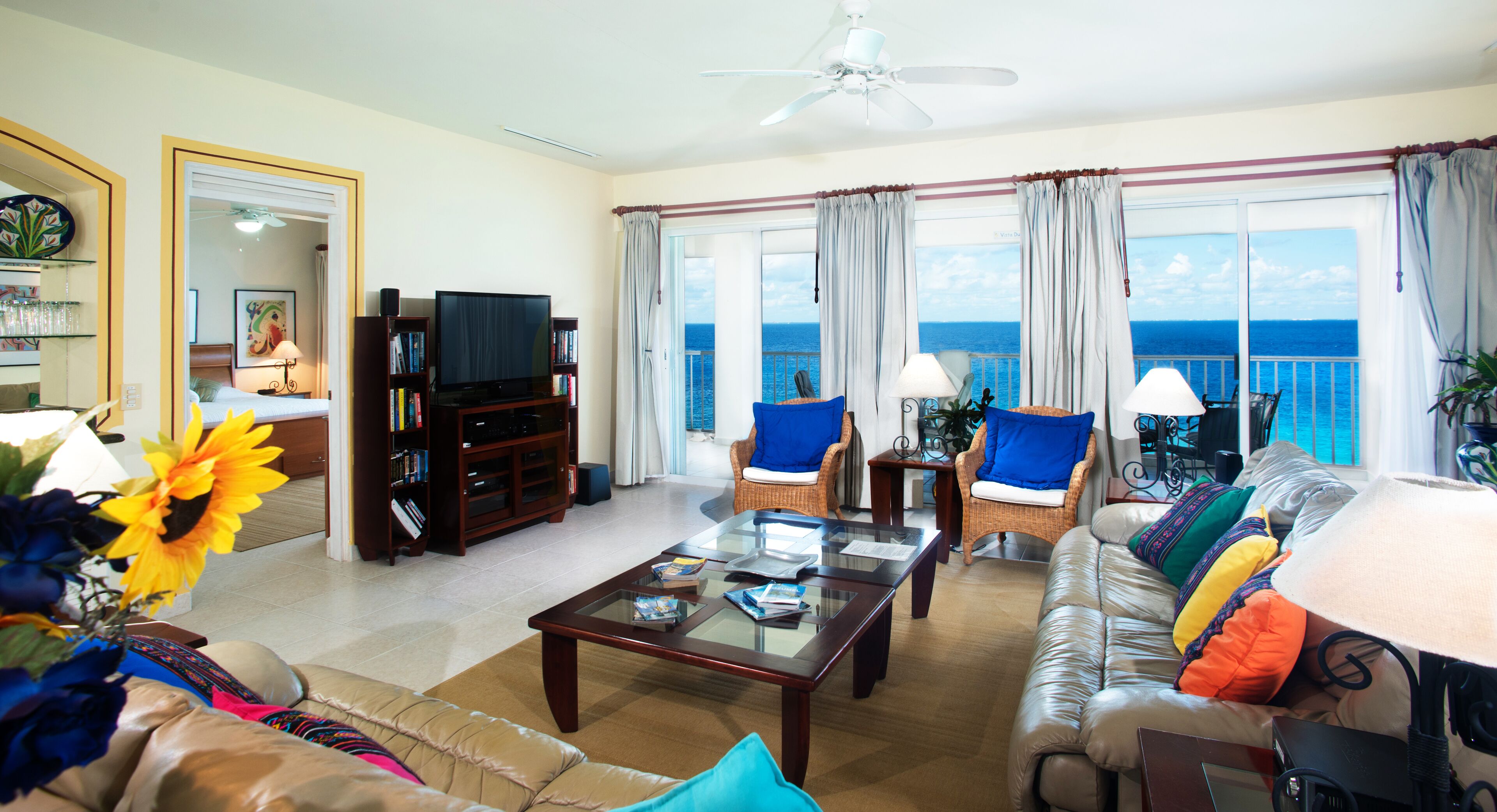 A spacious living room with a large window offering a view of the ocean, a television, and a bookshelf.