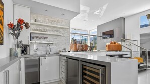 Une cuisine moderne avec des meubles blancs, un grand îlot central et un escalier en verre.