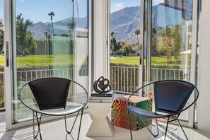 A balcony with two chairs, a decorative box, and a view of a golf course and mountains.
