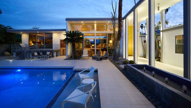 Une maison moderne dotée d’une piscine, d’un espace salon extérieur et de palmiers.