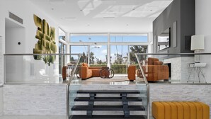 Un intérieur moderne avec un escalier, un coin salon doté de canapés orange et une grande fenêtre offrant une vue sur des palmiers.