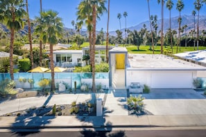 A modern building with a garage, surrounded by palm trees and a mountain view.