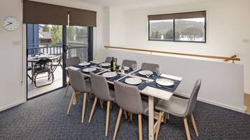 Uma sala de jantar com uma mesa posta para quatro pessoas, cadeiras, um relógio e uma janela com vista.