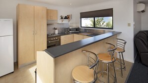 Eine moderne Küche mit Holzschränken, einem Edelstahlherd, einer Mikrowelle und einer Bar mit Hockern.