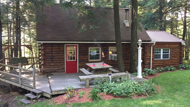 A rustic cabin with a red door, a deck, and a small outdoor table.