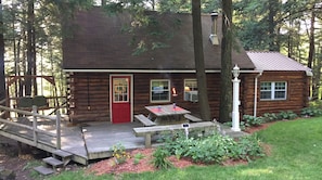 A rustic cabin with a red door, a deck, and a small outdoor table.