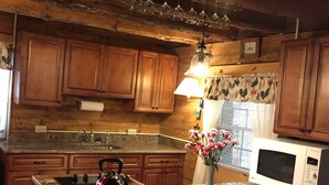 A kitchen with wooden cabinets, a granite countertop, a kettle, a microwave, and a vase with flowers.