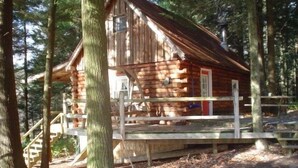 A rustic cabin with a wooden deck and stairs leading to the entrance.