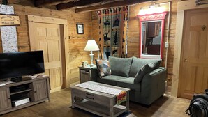 A cozy cabin interior with a television, a lamp, a sofa, and a wooden cabinet.
