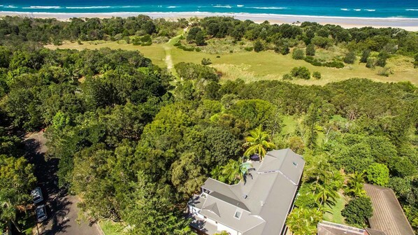 An aerial view of a property with a large house surrounded by dense greenery and a beach in the background. - Baby Blue - 3 BR villa steps from Tallow Beach (Byron Bay)