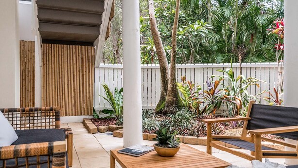 Un espace extérieur aménagé, abrité et doté de mobilier en bois et de plantes en pot.