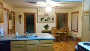 Cozy kitchen with central island, sink, and countertop, adjacent to a dining area with a wooden table and chairs.