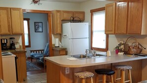 A compact kitchen with wooden cabinets, a white refrigerator, a sink, and a small island with bar stools.
