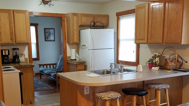 A compact kitchen with wooden cabinets, a white refrigerator, a sink, and a small island with bar stools.
