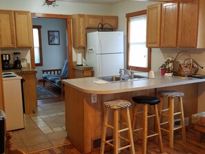 A compact kitchen with wooden cabinets, a white refrigerator, a sink, and a small island with bar stools.