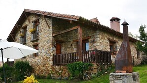 Una casa de piedra con balcón, chimenea y jardín con mesa y jarrón.