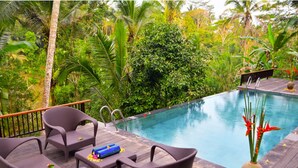 Una terraza de madera con mobiliario de mimbre y una piscina.
