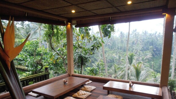 Una habitación con mesas y bancos de madera, ventanas amplias con vistas a un paisaje tropical.