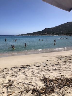 Ein Strand mit klarem, blauem Wasser und badenden Personen.