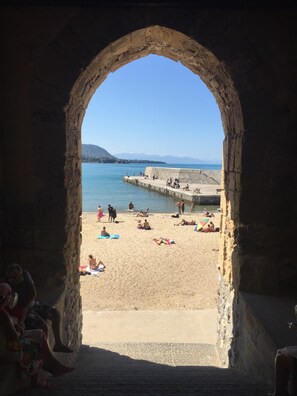 Une vue à travers une arche donnant sur une plage où des gens se prélassent au soleil et se baignent.