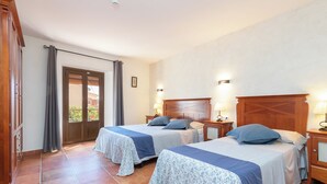 Een hotelkamer met twee bedden, een houten hoofdbord, een klein nachtkastje met een lamp en een deur die uitkomt op een buitenruimte.