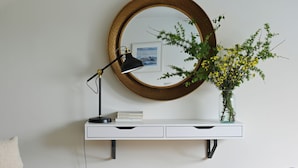 A modern living room with a grey sofa, a small side table, a white console table with a mirror and a vase of flowers, and a lamp. - Historic Townhouse in Clifden with courtyard+ balcony overlooking
Clifden Bay (Clifden)