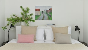 A neatly made bed with a striped blanket, a white pillow, and two beige pillows. There is a small table with a vase of flowers and a painting on the wall. - Historic Townhouse in Clifden with courtyard+ balcony overlooking
Clifden Bay (Clifden)