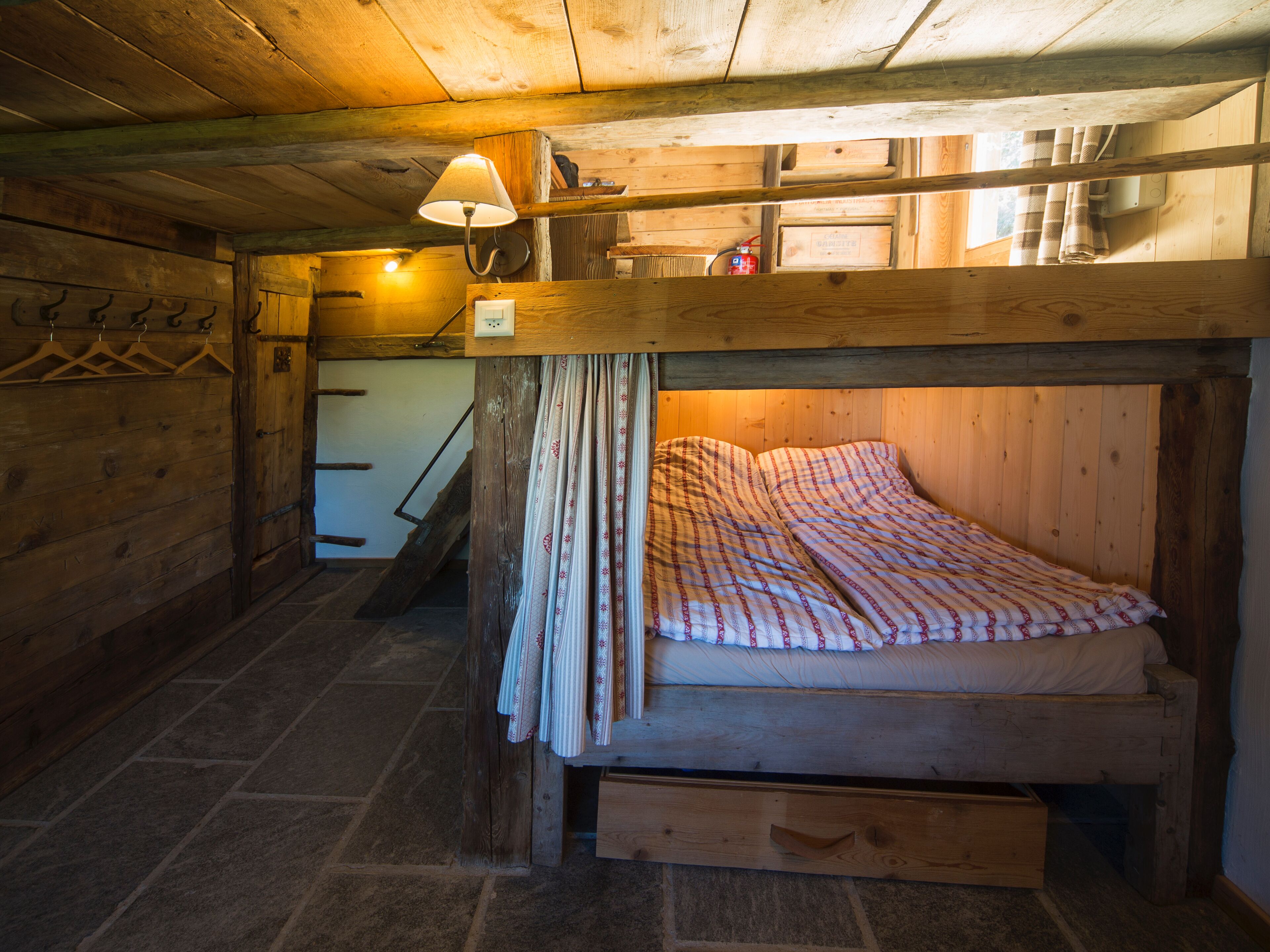 Una camera rustica in legno con un letto a castello, una piccola scrivania, una lampada e una scala.