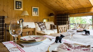Ein gemütliches Holzhaus-Interieur mit einem Esstisch, gedeckt für zwei Personen, inklusive Weingläsern, Tellern und einer kleinen Hundfigur.