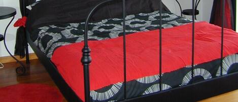 Un lit avec un cadre en métal noir, une couvre-lit rouge et des rideaux noirs transparents.
