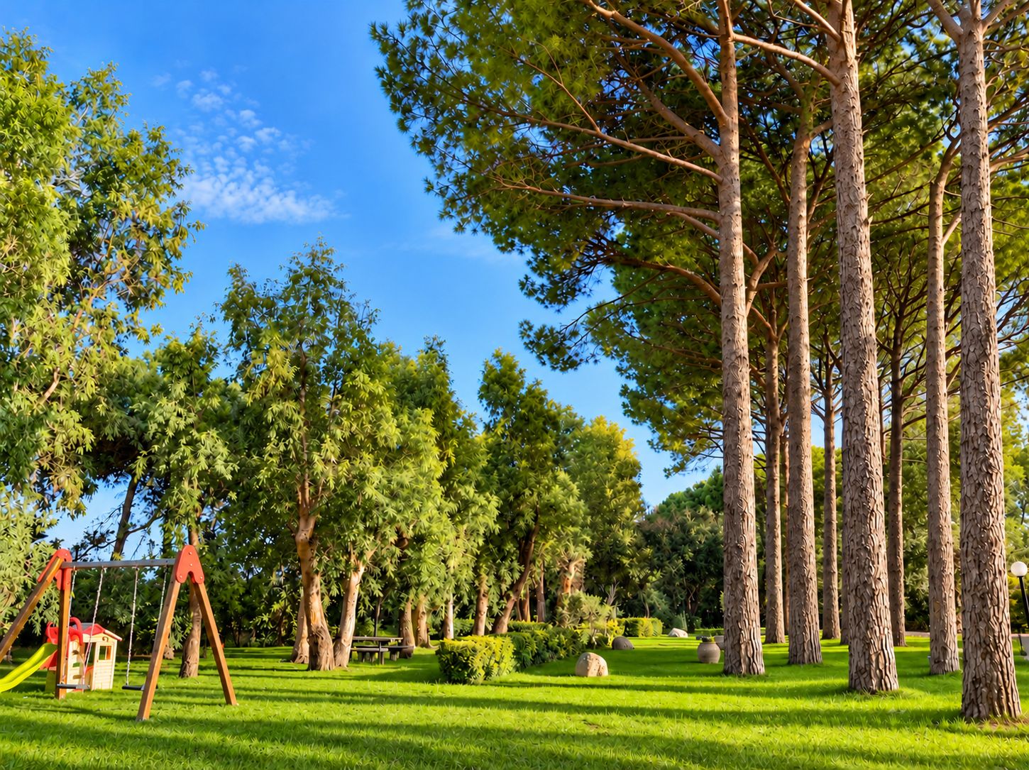 A park with a swing set, trees, and a well-maintained lawn.