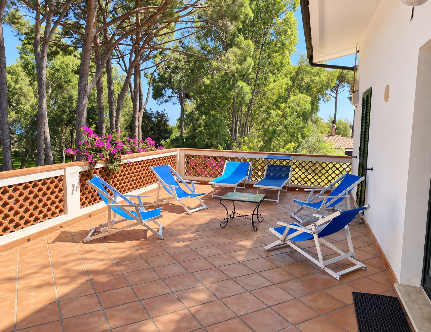 A terrace with blue lounge chairs, a table, and a decorative fence.