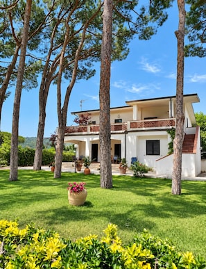 A two-story house with a balcony, surrounded by trees and a well-maintained lawn. -  Beachfront Villa with spacious garden and direct beach access  (San Sostene Marina)