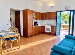 A compact kitchen with wooden cabinets, a dining table with chairs, and a sofa. -  Beachfront Villa with spacious garden and direct beach access  (San Sostene Marina)