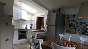 Una cocina moderna con armarios blancos, un refrigerador de acero inoxidable y un comedor con mesa de madera y sillas blancas.