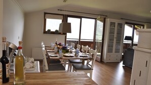 Un comedor con una mesa de madera dispuesta para cuatro personas, rodeada de sillas blancas. Se observa un aparador con puertas de vidrio al fondo.