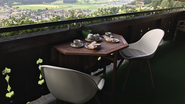 Un balcón con una mesa dispuesta para tomar té, dos sillas y una vista panorámica de un valle.