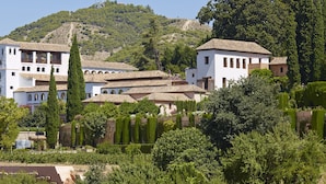 Un edificio tradicional con varios balcones y techo de tejas, rodeado de vegetación exuberante y un paisaje de colinas.