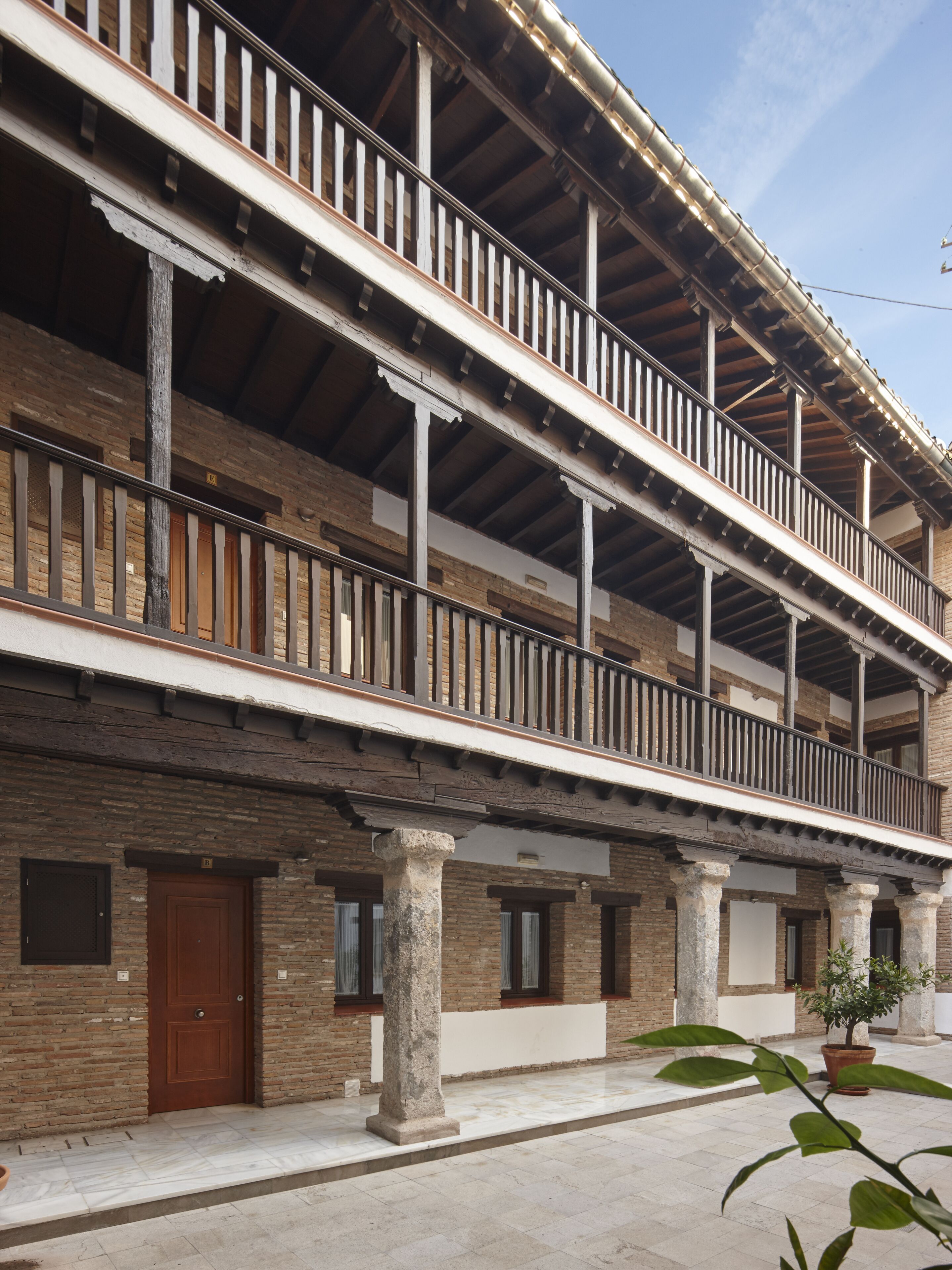 A multi-story building with a balcony, stone columns, and a tiled ground floor.