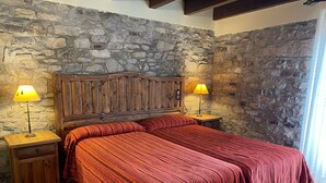 Un dormitorio con pared de piedra, cabecero de madera, dos mesitas de noche con lámparas y una cama con ropa de cama a rayas.