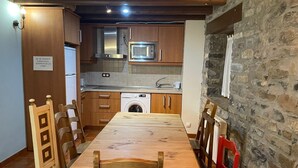 Una cocina compacta con armarios de madera, microondas integrado, lavadora y una pared de piedra.