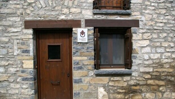 Un edificio de piedra con puerta y ventana de madera, y un letrero sobre la puerta.